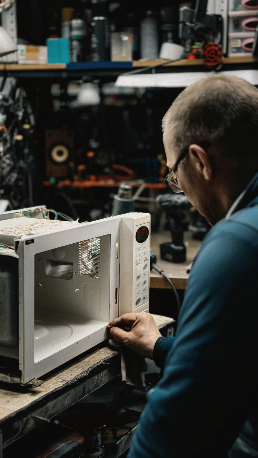 A technician examining the inside of a microwave on a bench